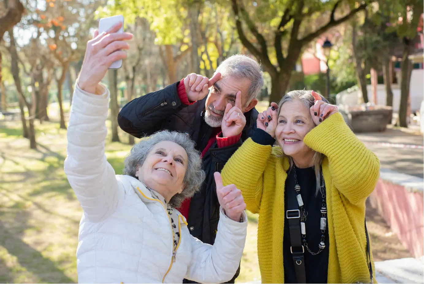 Three older adults taking a cheerful selfie outdoors in a park