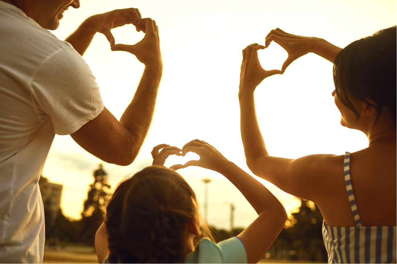A family making heart shapes with their hands at sunset